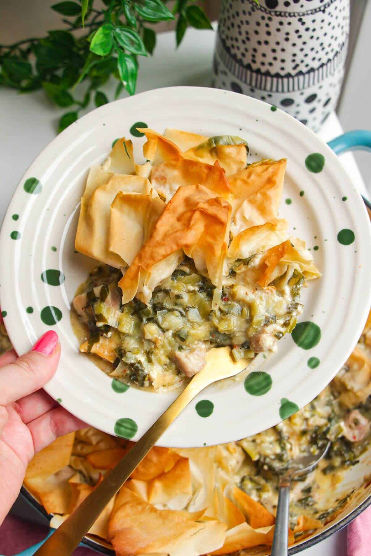 Spanokopita chicken pot pie on plate with hand holding.