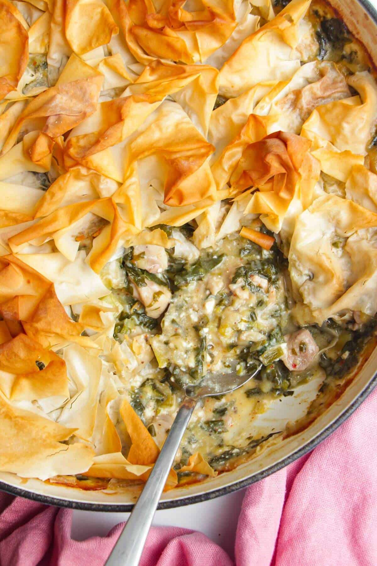 Spanokopita chicken pot pie, with a serving spoon in the pan.