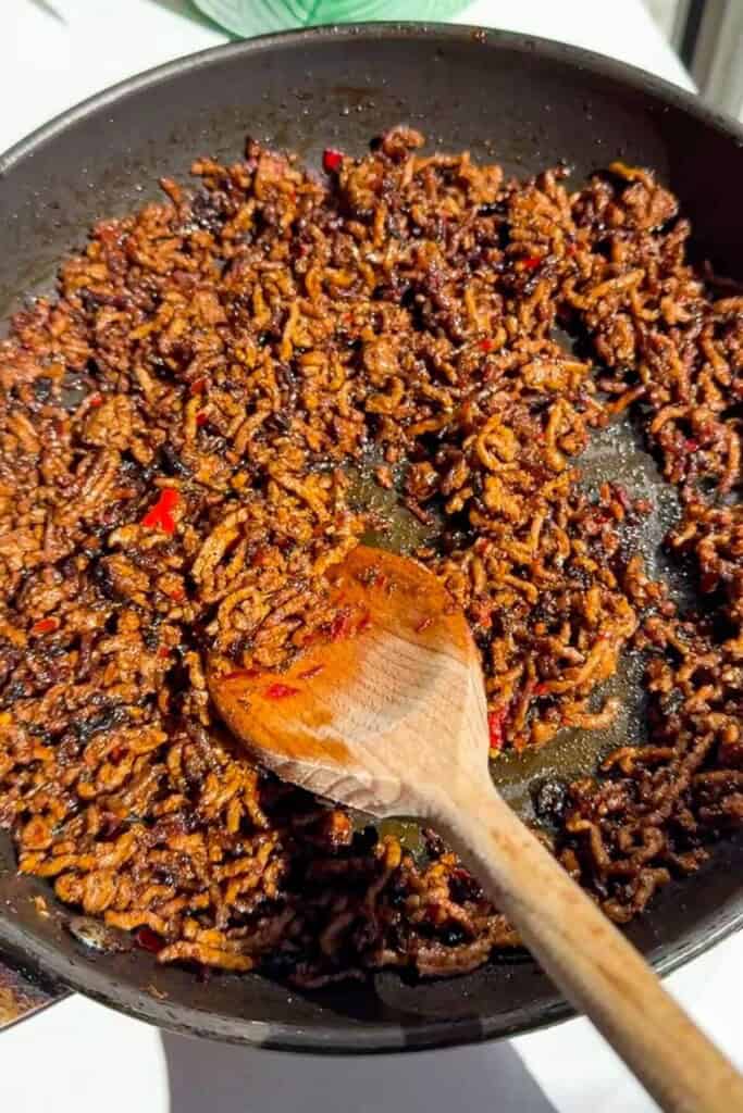 Stirring sticky ground beef in pan.