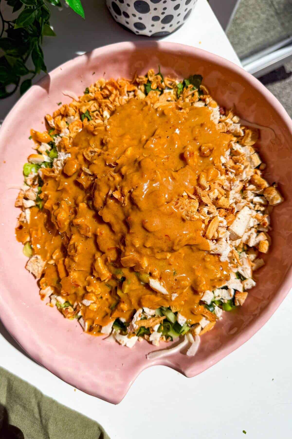Satay dressing poured over salad in large mixing bowl.