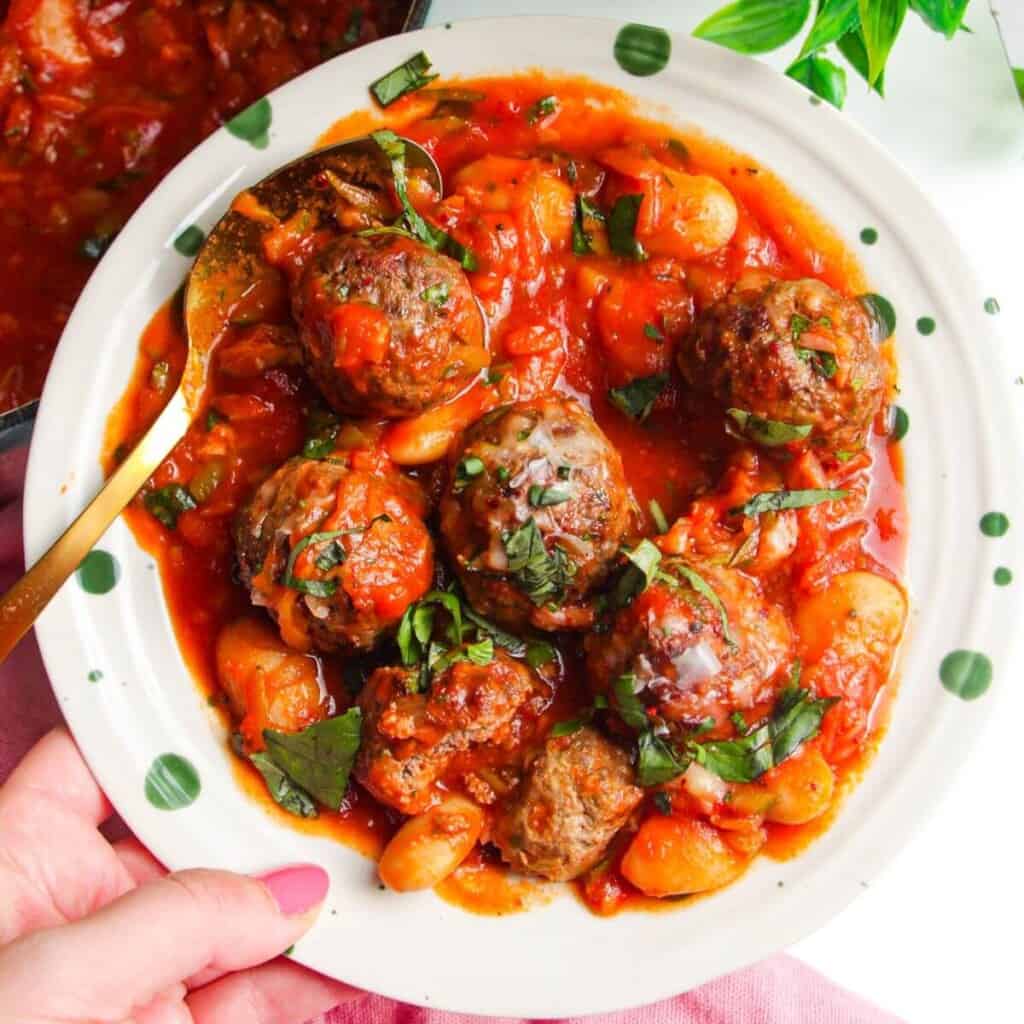 Holding plate with beef meatballs and butter beans in tomato sauce.