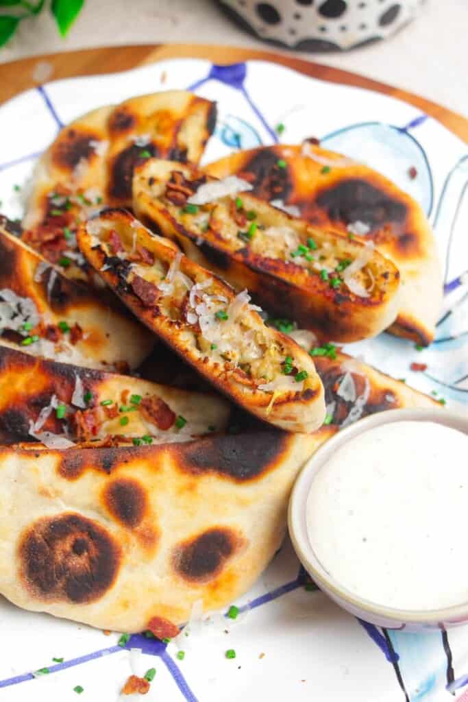 A pile of Caesar stuffed flatbreads on a platter with Caesar dip on the side.