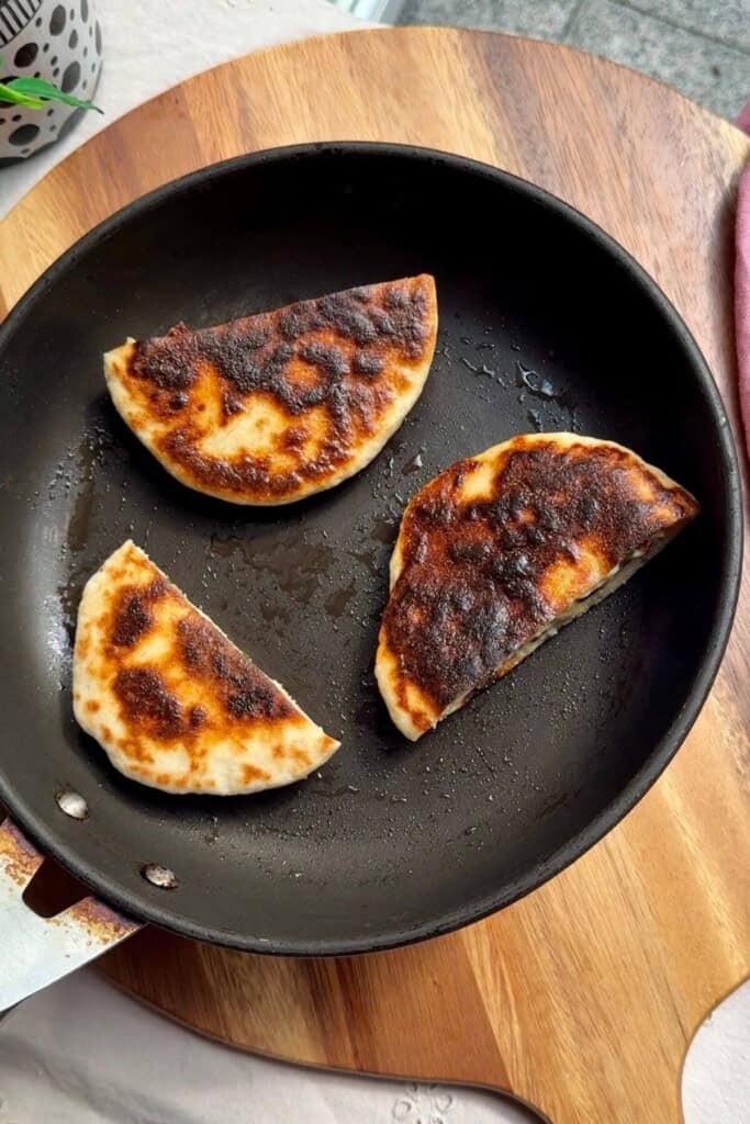 Three flatbreads cooking in a hot pan.