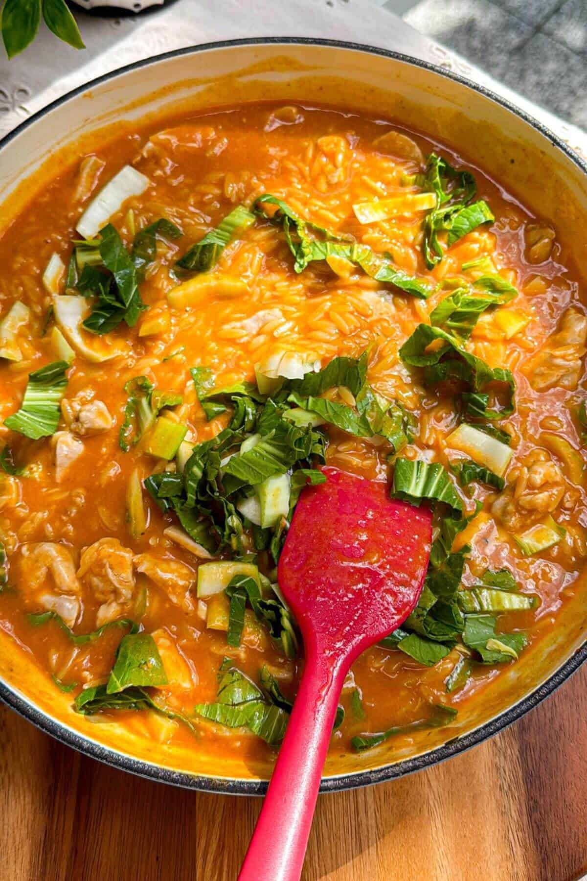 Pak choi added to red curry orzo in a pan.
