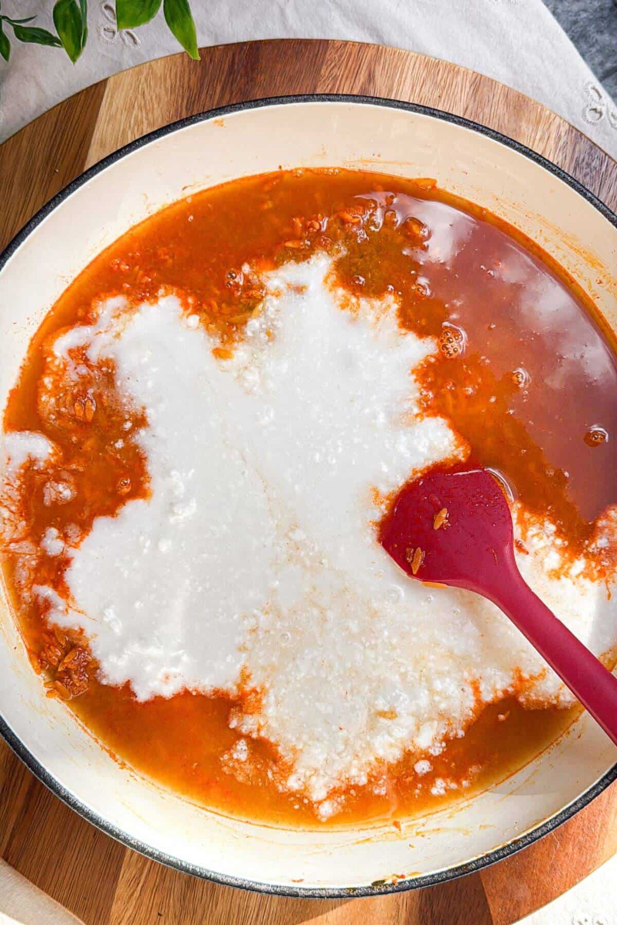 Coconut milk and stock added to red curry paste and orzo in a pan.