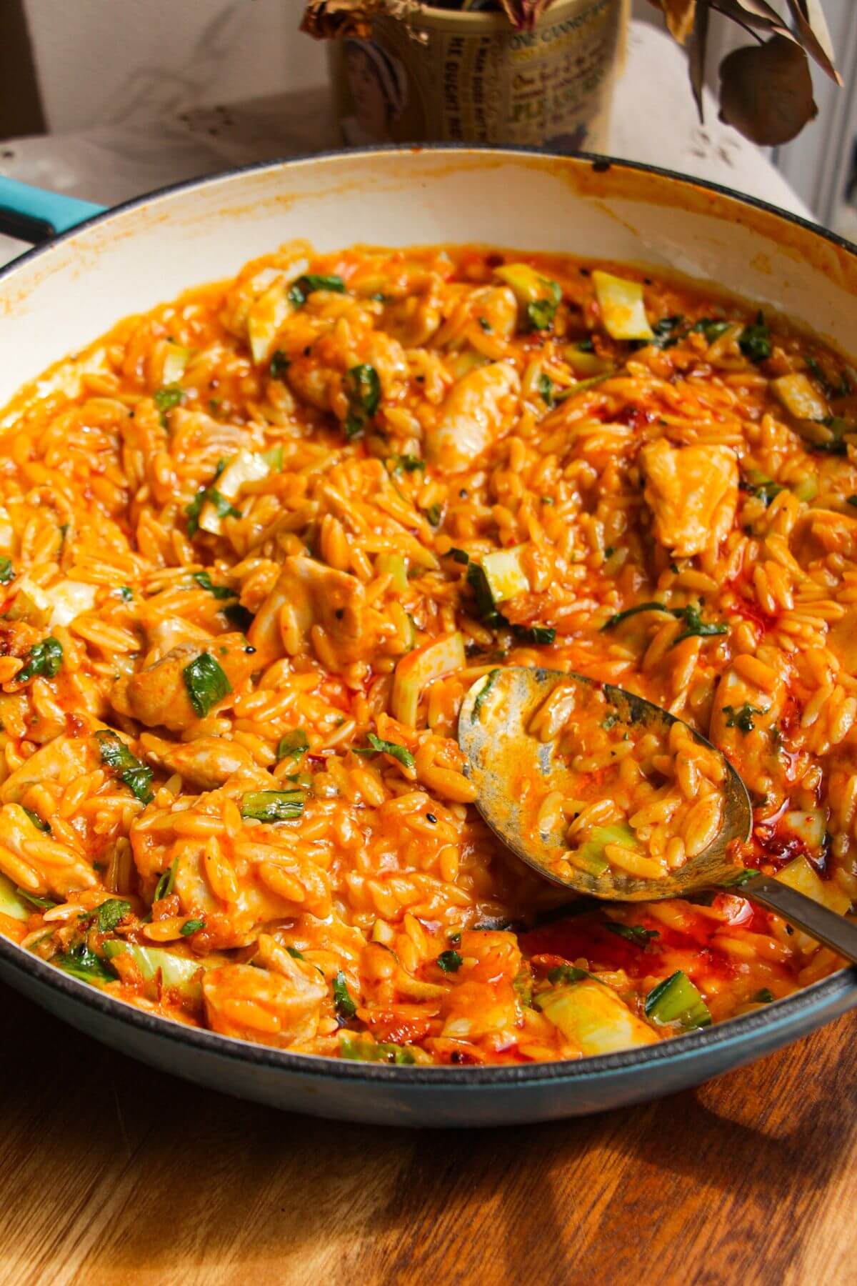 Red curry chicken orzo in a pan with a spoon.