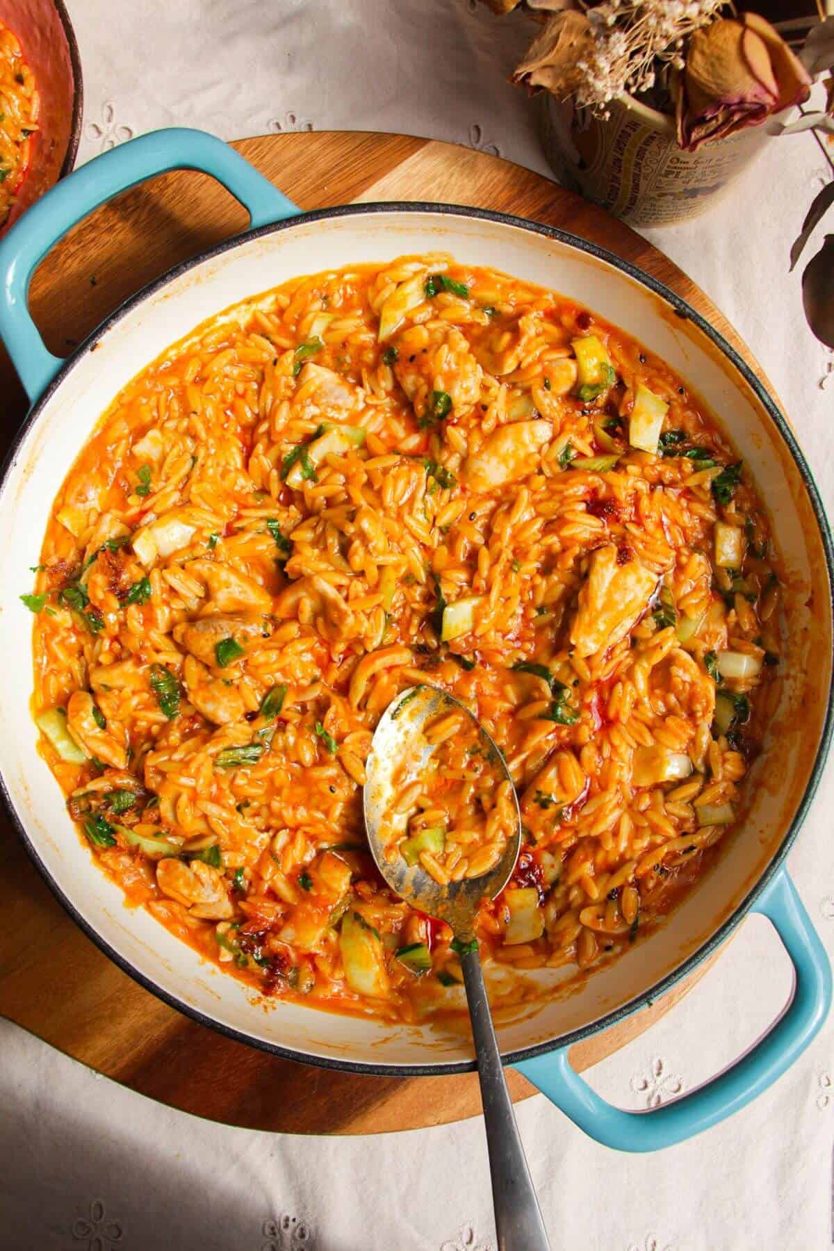 Red curry chicken orzo in a pan with a spoon.