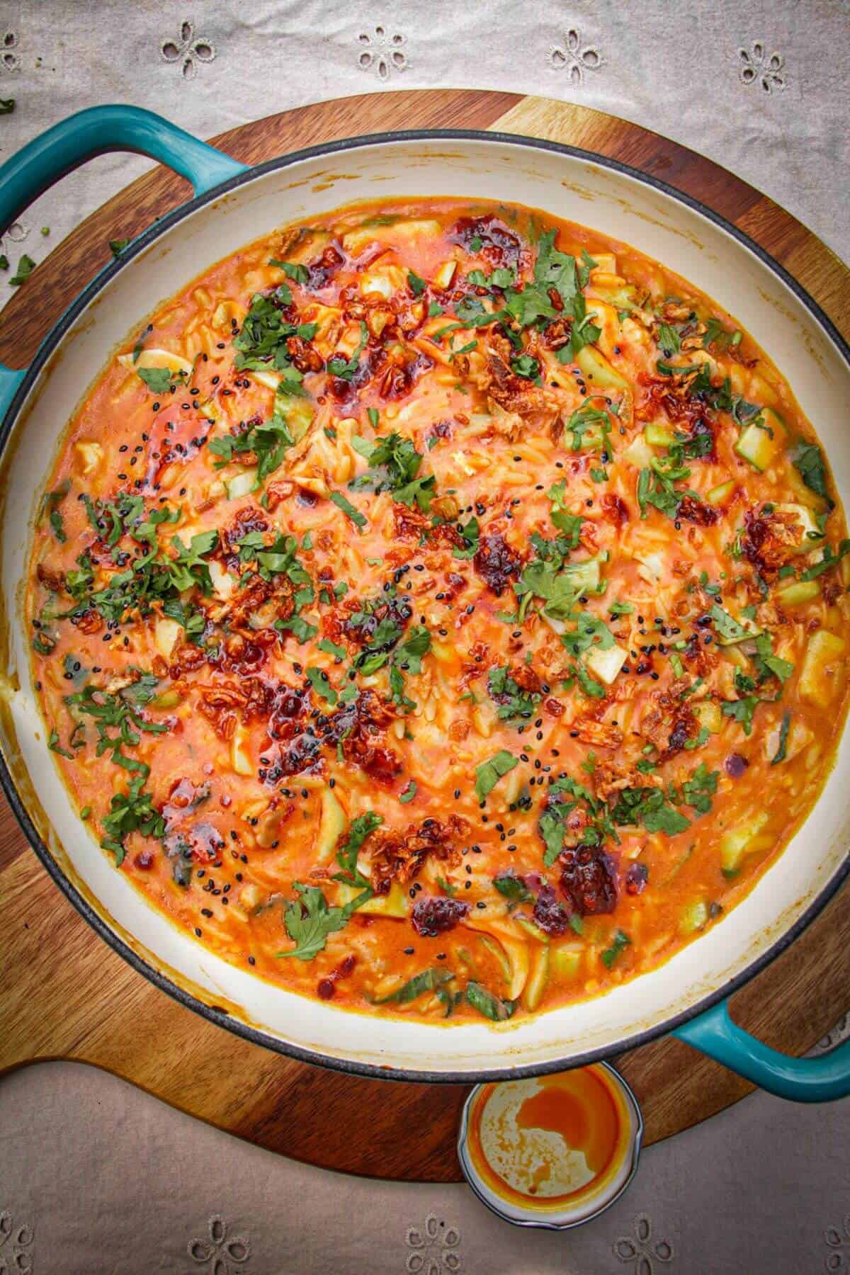 Red curry chicken orzo in a pan, drizzled with chili oil.