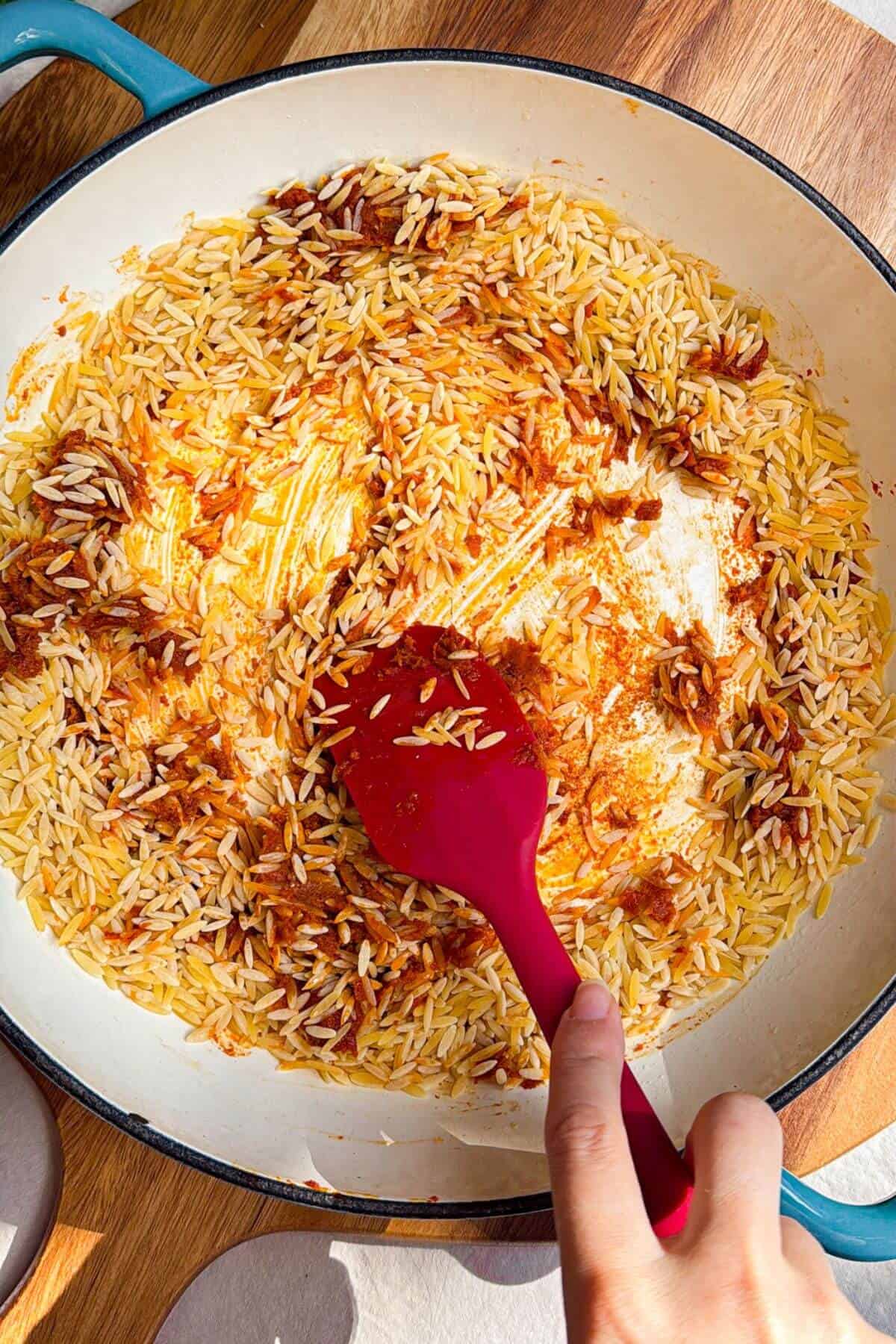 Orzo being mixed through red curry paste in a pan.