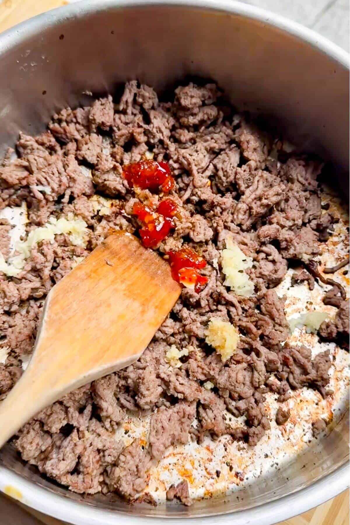 Sweet chili, ginger, and garlic added to ground beef in a pan.