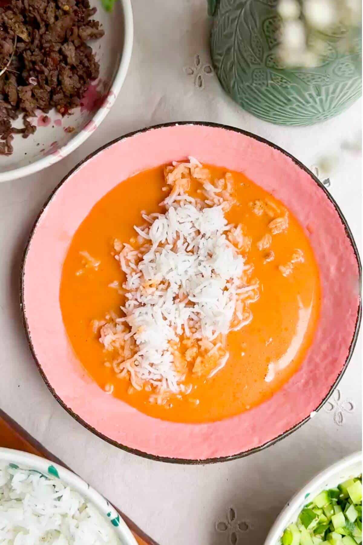 Gochujang broth spooned over rice in a pink bowl.
