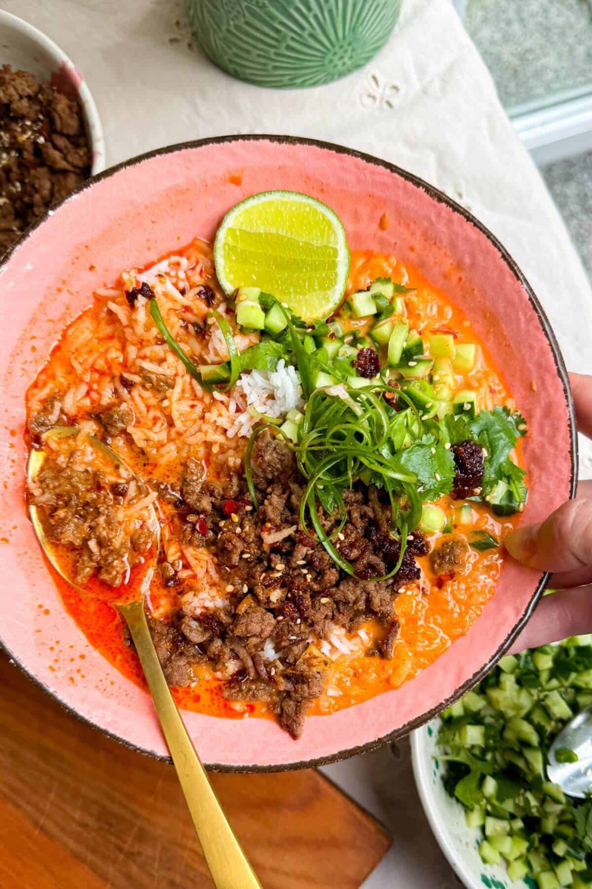 Sticky beef, rice, scallions in a pink bowls with orange gochujang broth.
