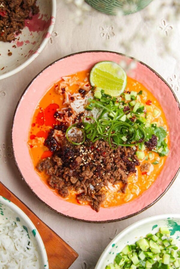 Sticky beef, rice, scallions in a pink bowl with orange gochujang broth.